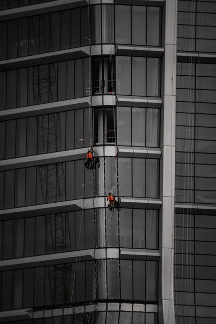 A window cleaner using a squeegee to clean a glass building facade on a cloudy day.